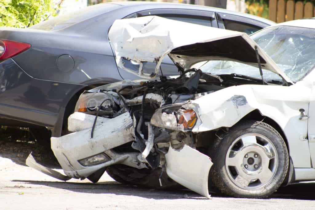 Damaged white car with a crumpled front end parked next to a gray car.