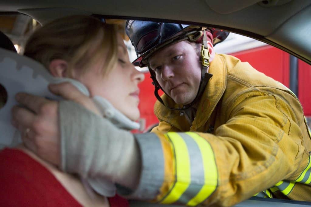 A firefighter supports a woman in a car by placing a cervical collar around her neck, ensuring her safety during an emergency response.