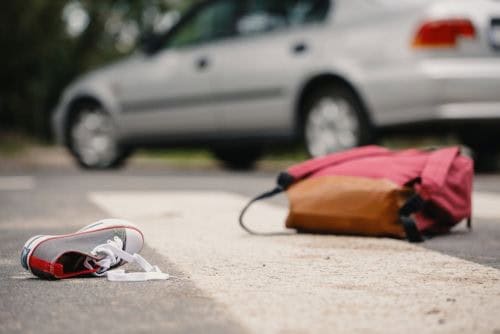 A sneaker and a backpack lie on a crosswalk with a parked car in the background.