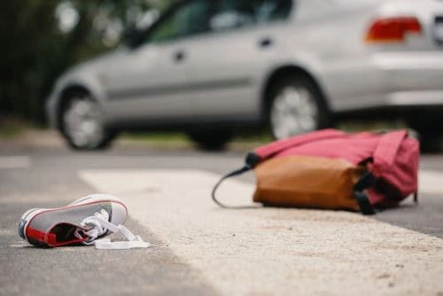 A sneaker and a backpack lie on a crosswalk, with a blurred car in the background.