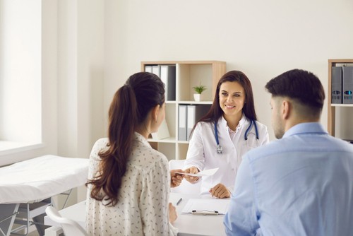 A doctor hands a prescription to a woman while a man sits beside her in a medical office.